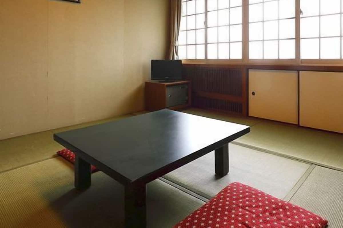 Um espaço com tatames, uma mesa baixa, uma televisão e uma porta deslizante.