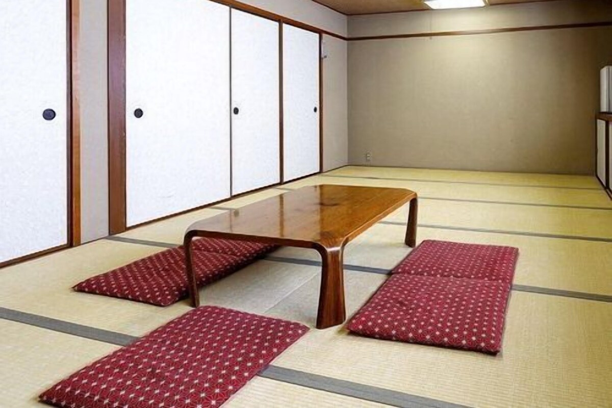 Una habitación con esterillas de tatami, una mesa de madera y cojines rojos.
