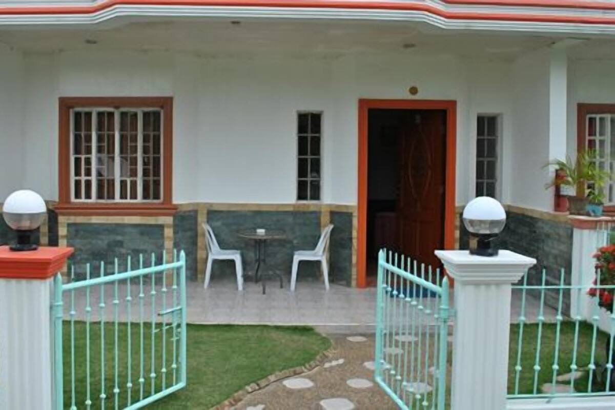 Un edificio con un patio techado, sillas blancas y una pequeña mesa.