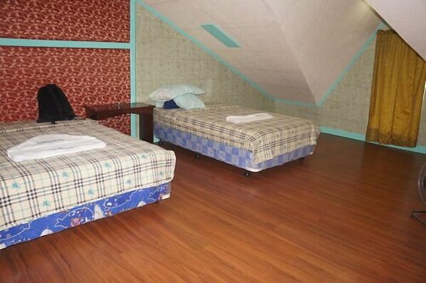 A small, cozy room with two beds, wooden flooring, and a sloped ceiling. - Datag Cordova Home Village (Cordova)