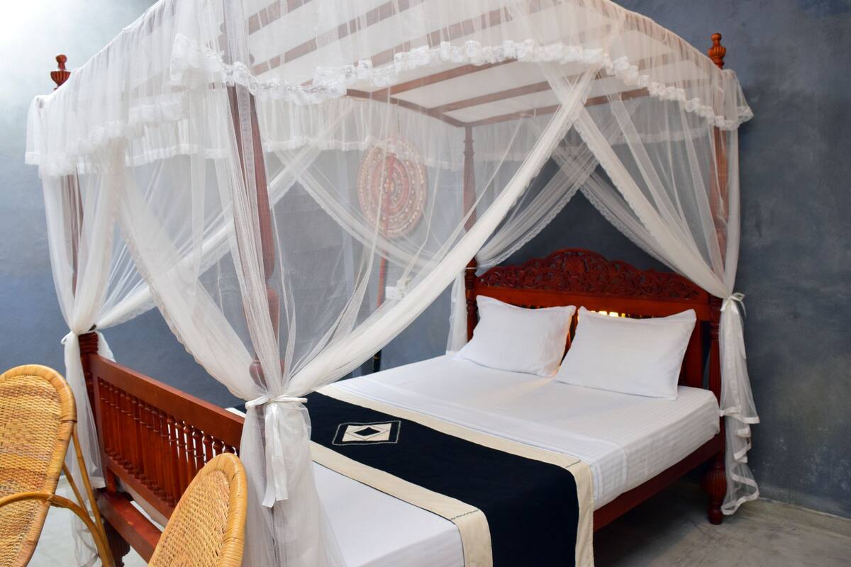 Una cama con dosel y cuatro columnas, con ropa blanca y un plaid oscuro.