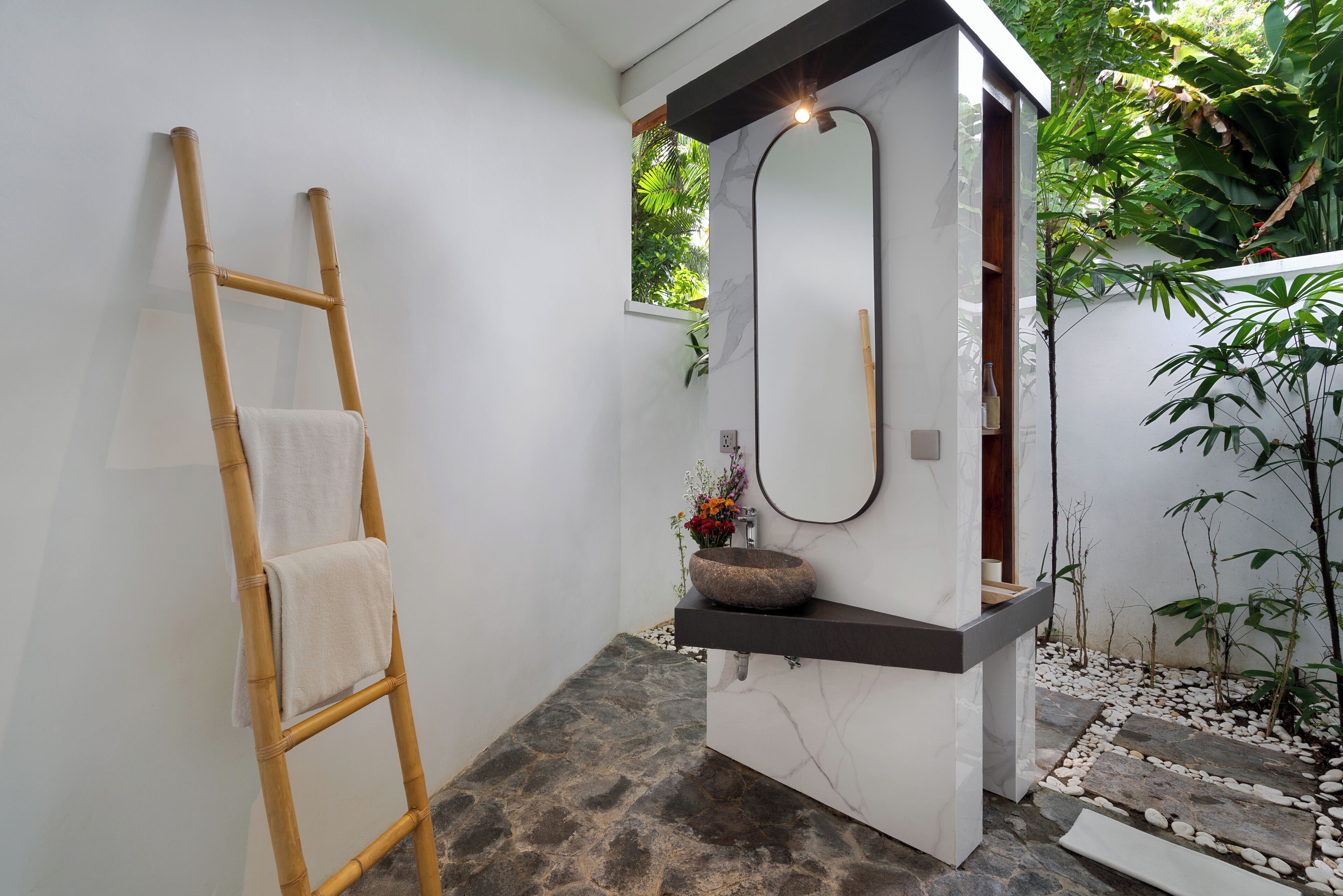 Un baño con suelo de piedra, una escalera de madera con una toalla, un lavabo de piedra y un espejo grande.