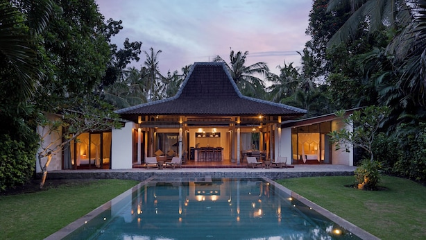 Una casa moderna con piscina, rodeada de exuberante follaje y palmeras.