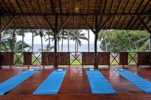 Terraza de madera con tapetes de yoga azules y vista al océano y palmeras.