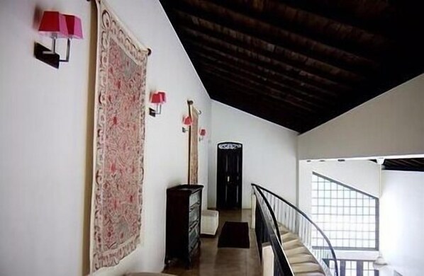 Un corridoio con un ampio tappeto a motivi, una scala con ringhiera nera e una porta con maniglia decorativa.