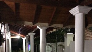 An outdoor patio area with wooden tables and chairs, surrounded by white pillars and potted plants. - Sunrise Palace (Negombo)