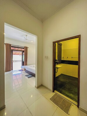 Une chambre d’hôtel avec un balcon, une salle de bain aux carreaux jaunes et un ventilateur de plafond.