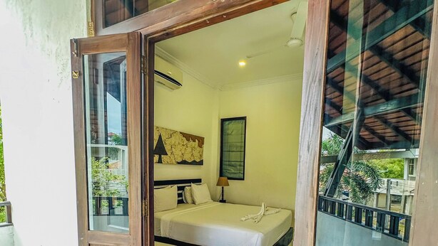 A room with a wooden door leading to a bedroom with two beds, a map on the wall, and a view of greenery outside. - Sunrise Palace (Negombo)