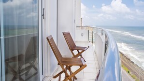 Un balcon avec deux chaises en bois, une porte vitrée et une vue sur l’océan.