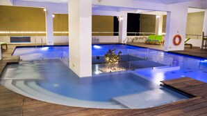 Une piscine intérieure dotée de plusieurs couloirs, d’une zone de pont en bois et d’un salon avec un fauteuil vert et une bouée accrochée au mur.