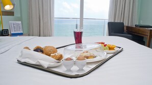 Un plateau de petit-déjeuner soigneusement préparé, posé sur un lit d’où l’on peut admirer la mer.