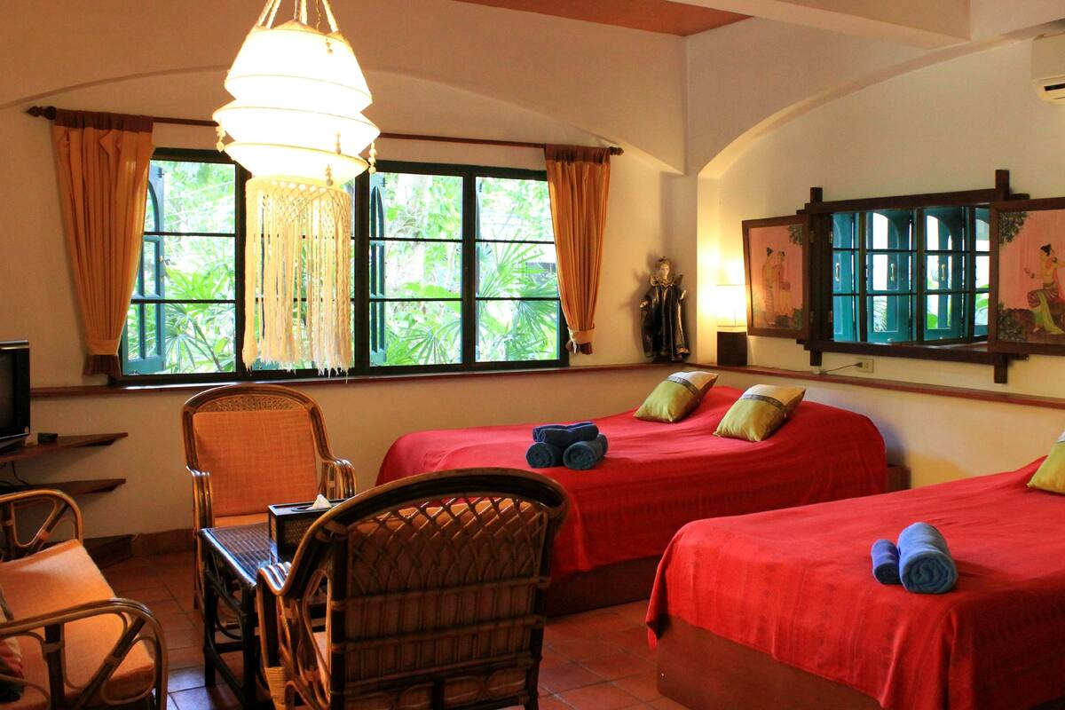 A hotel room with two beds, a desk with a chair, a television, and a large window with curtains.