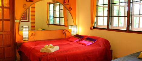 A bedroom with a large bed, a mirror, and a window with curtains.