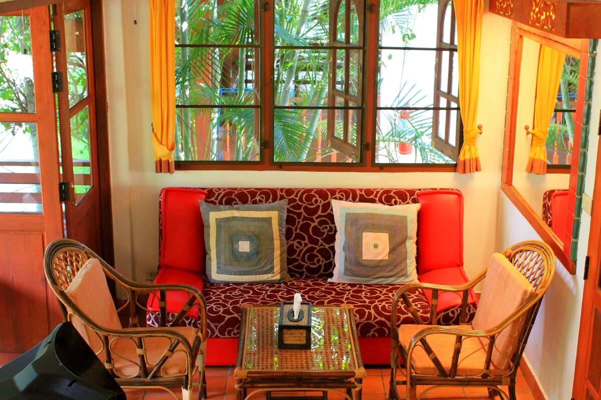 A room with a red sofa, two wicker chairs, a small table, and a window with curtains.