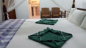 A neatly made bed with a checkered blanket and two folded green towels. There are two wooden chairs and a small table in the background. - Akash Villa (Thalaramba)