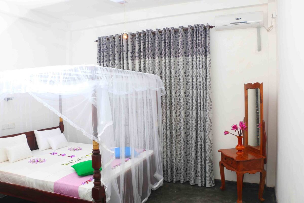 A neatly arranged bedroom with a bed, a bedside table, a mirror, and a curtain.