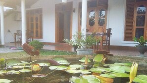 A serene pond with lily pads and a wooden table and chairs in the background. - Akash Villa (Thalaramba)