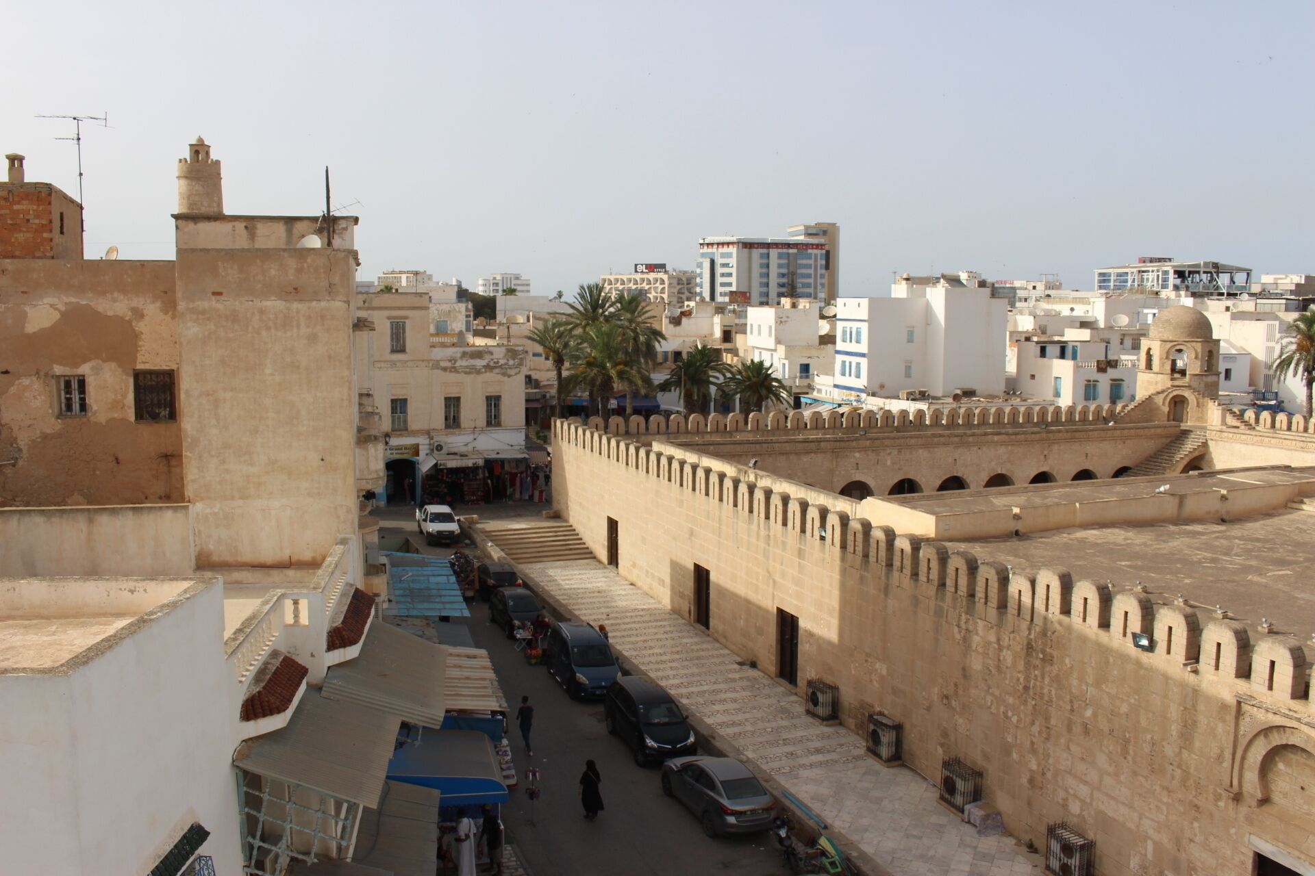 Vista de la calle con un muro fortificado, coches estacionados y edificios con balcones.