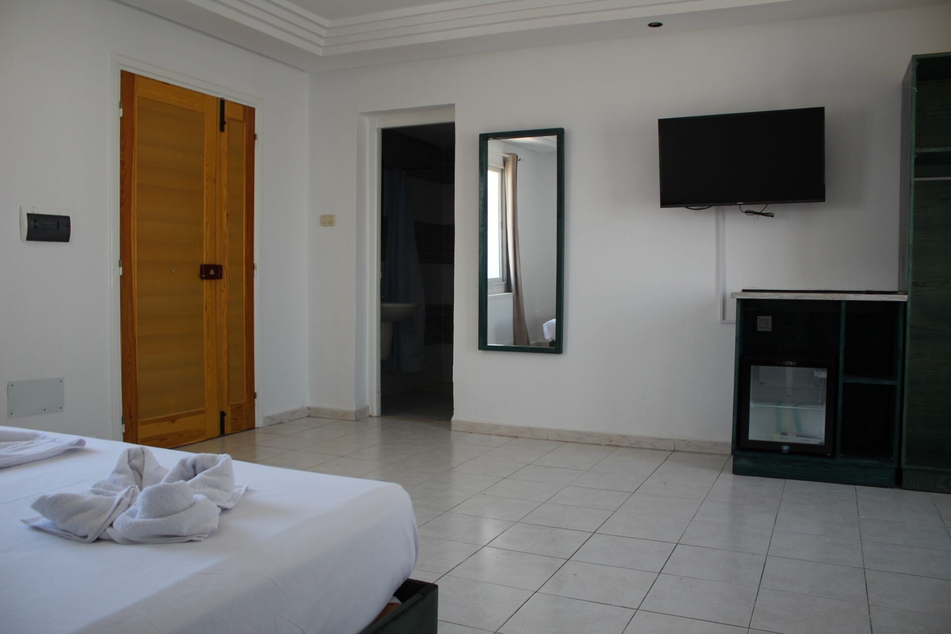 A hotel room with a bed, a TV, a mirror, and a wardrobe.