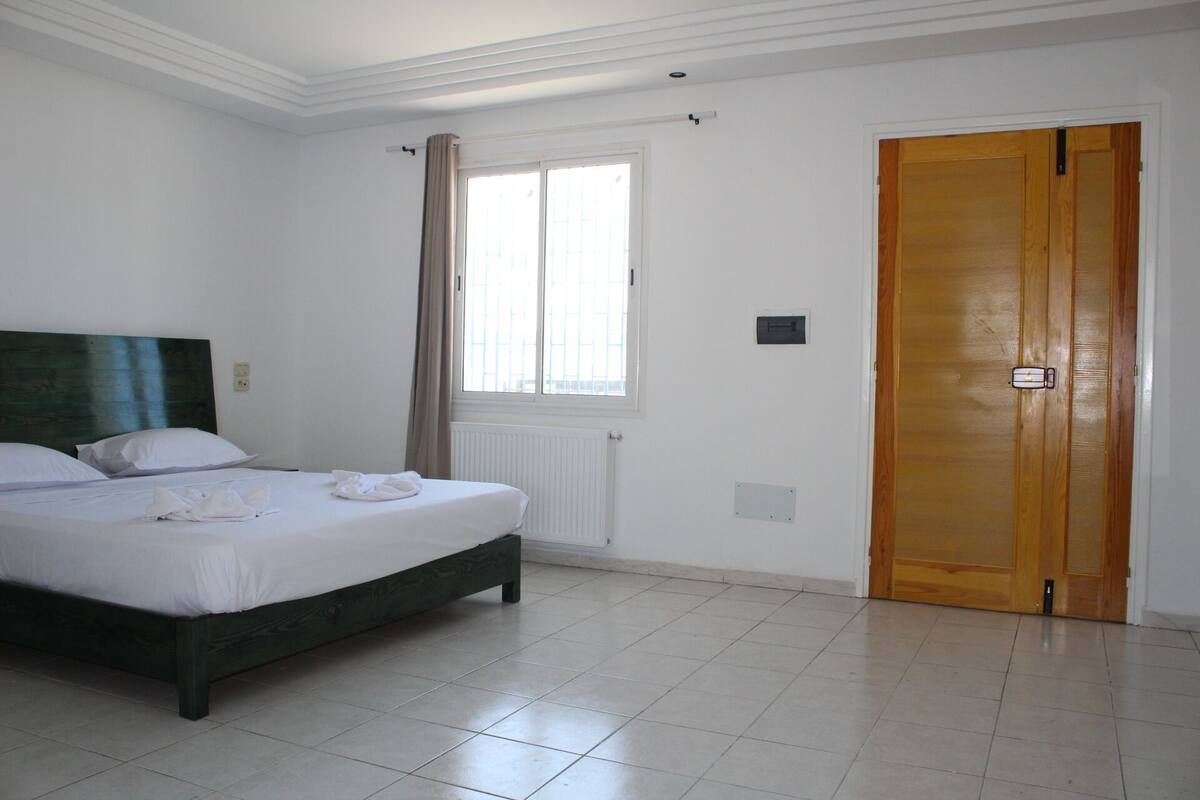 A bedroom with a bed, a window with curtains, a radiator, and a wooden door.