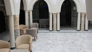 A courtyard with marble flooring, white arches, and beige armchairs. - Hôtel Medina (Sousse)