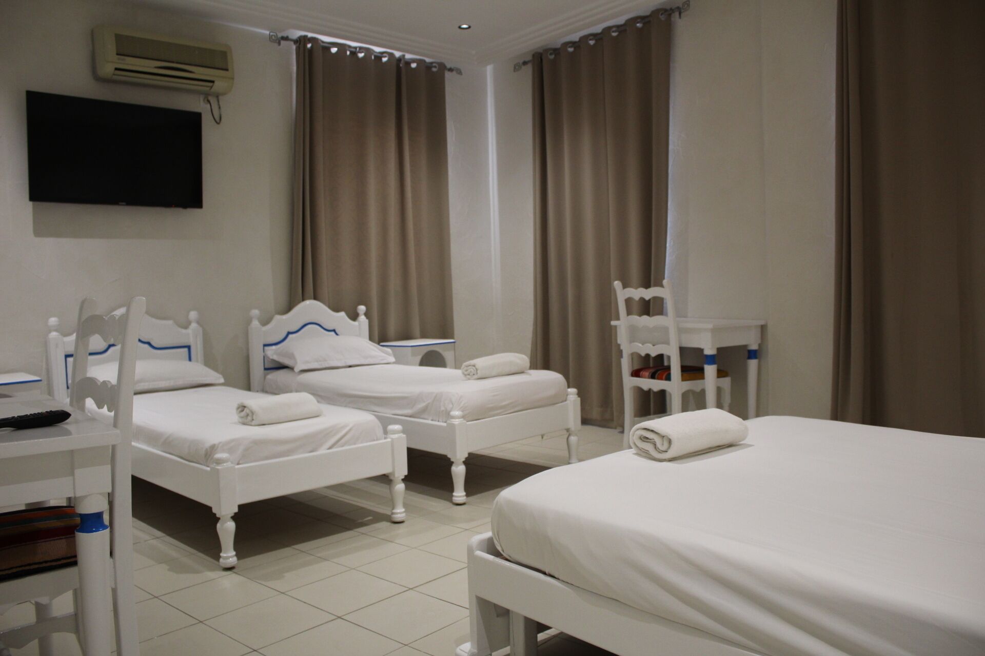 A hotel room with two single beds, a TV mounted on the wall, and a small table with a chair.
