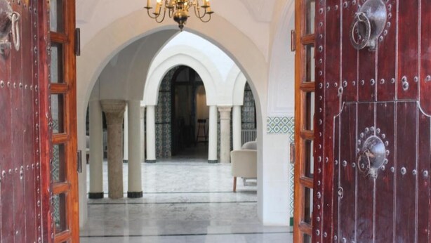 A grand entrance with a chandelier, arched columns, and a red door with metal studs. - Hôtel Medina (Sousse)