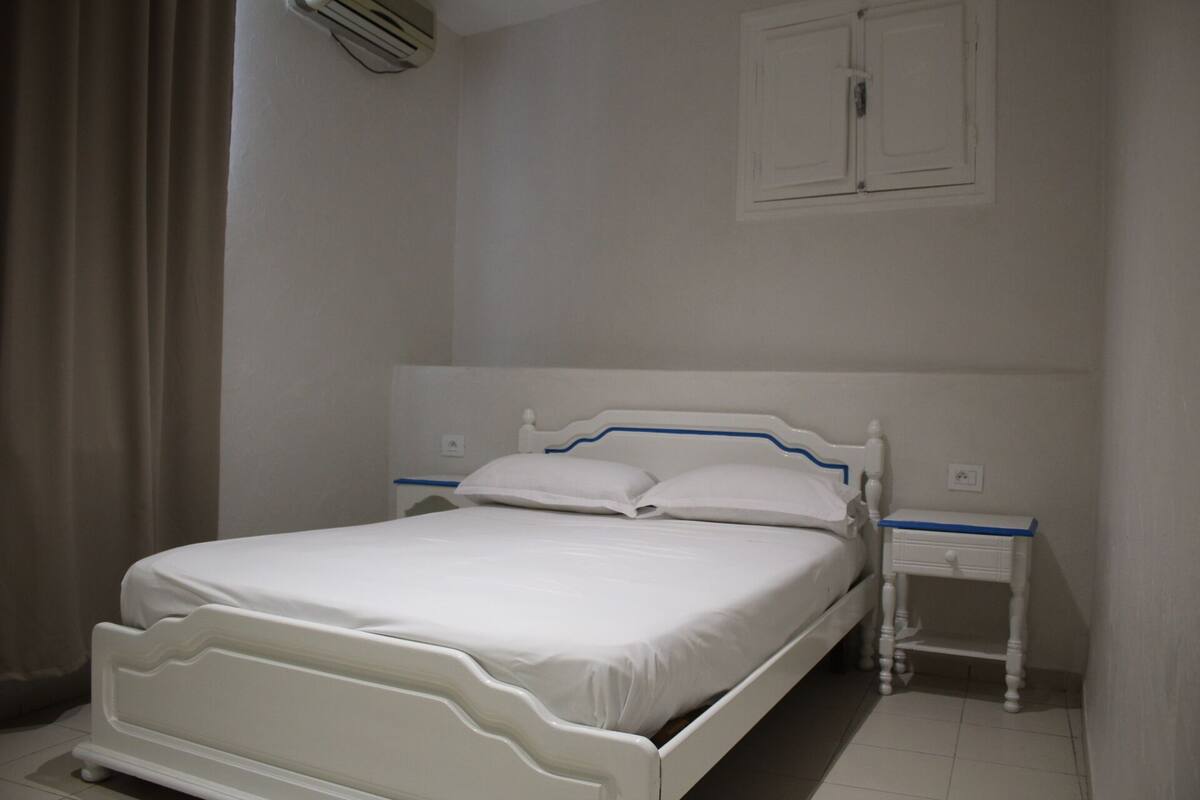 A white bed with a headboard, two bedside tables, and a wall-mounted cabinet.