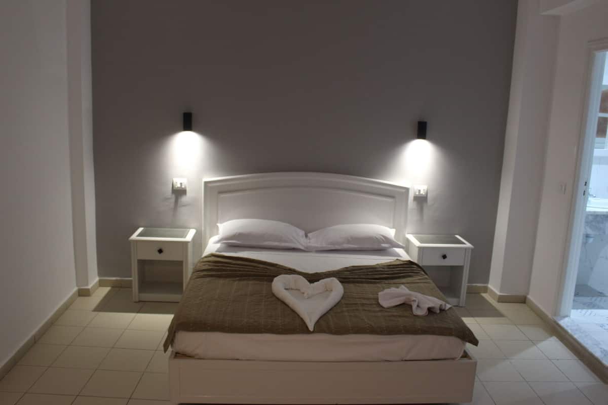 A neatly made bed with a heart-shaped towel, two bedside tables, and wall-mounted lights.