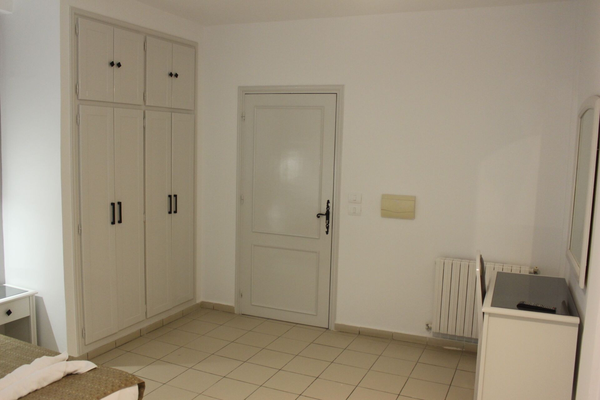 A room with a wardrobe, a door, a radiator, and a small table.