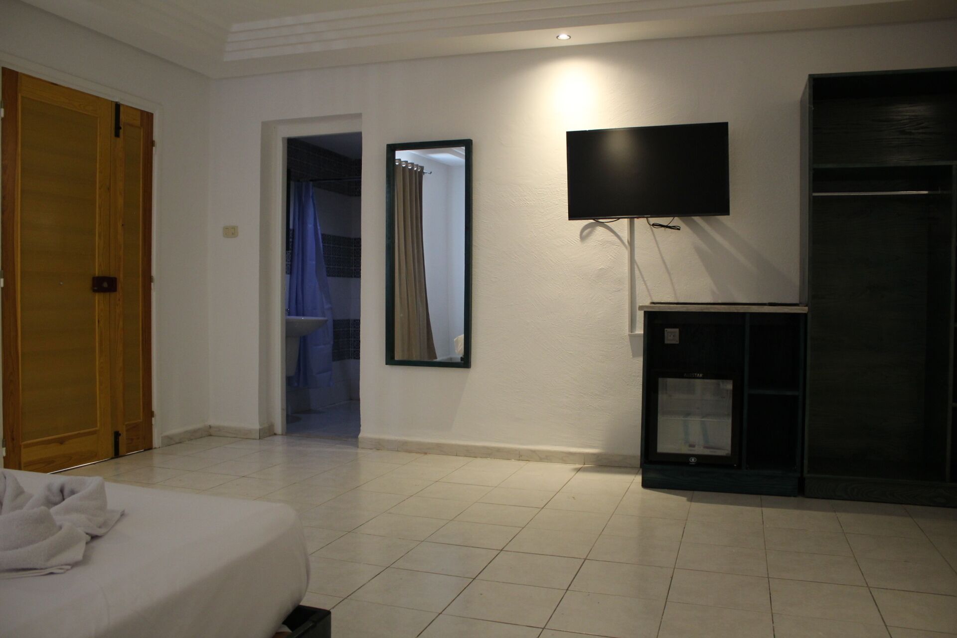 A hotel room with a bed, a TV mounted on the wall, a wardrobe, and a bathroom visible through an open door.