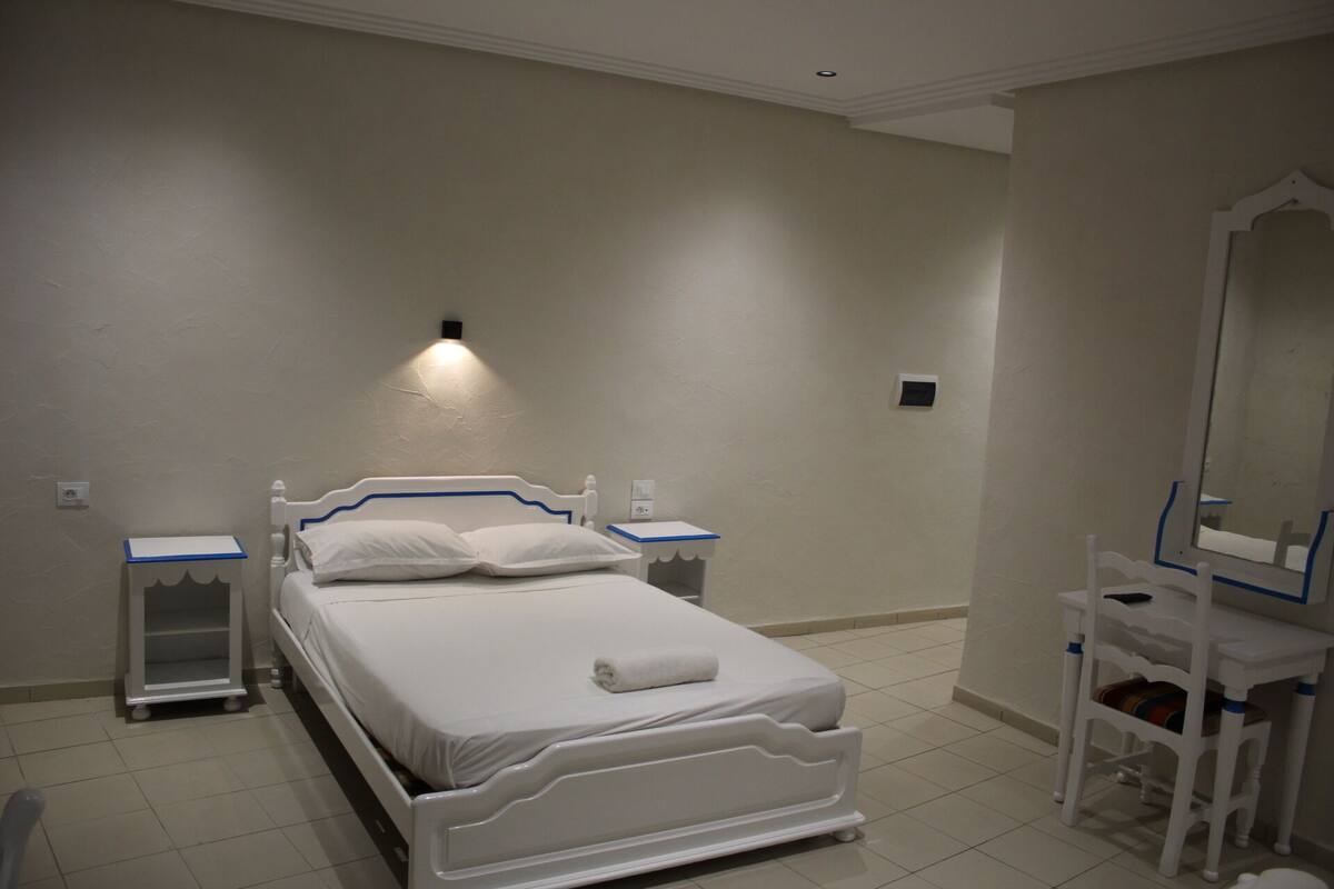A hotel room with a bed, bedside tables, a chair, and a mirror.