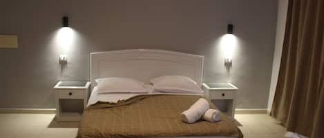 A neatly made bed with a brown blanket and white pillows, two bedside lamps, and a curtain on the right.
