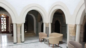 A spacious interior with white arches and a marble floor, featuring two beige armchairs and a small table. - Hôtel Medina (Sousse)