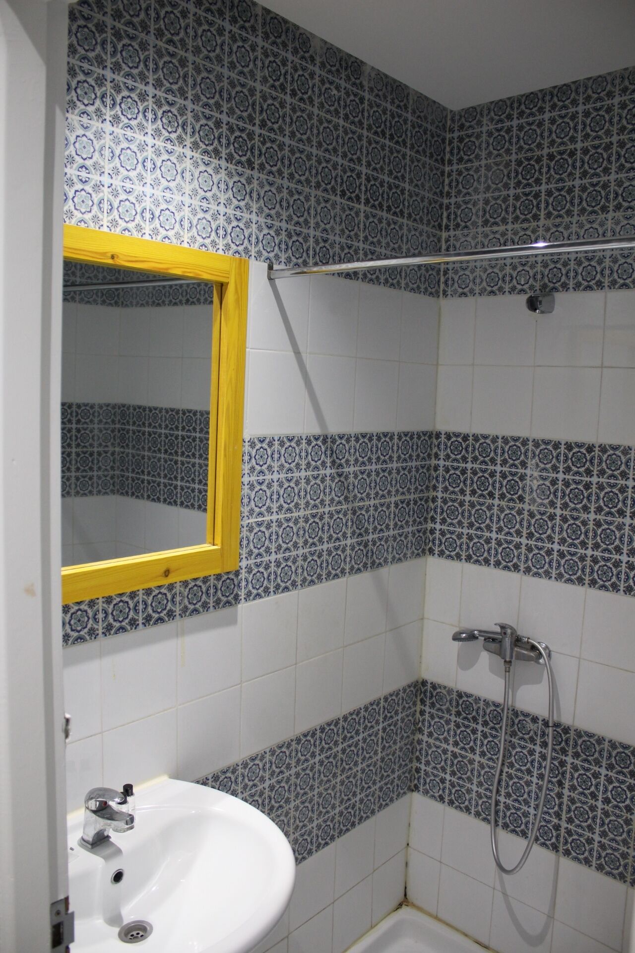 Un bagno con piastrelle decorate, un lavandino bianco, uno specchio con cornice gialla e una zona doccia.