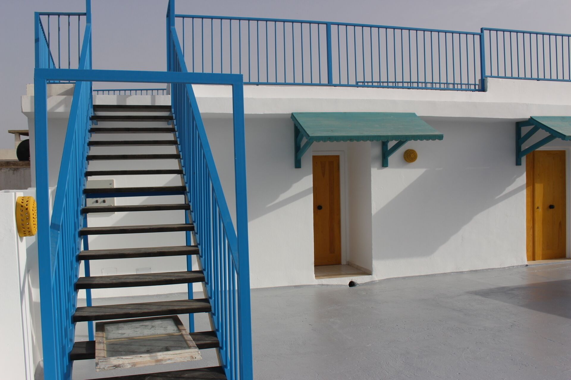 A staircase with blue railings leading to a building with white walls and green awnings over doors.