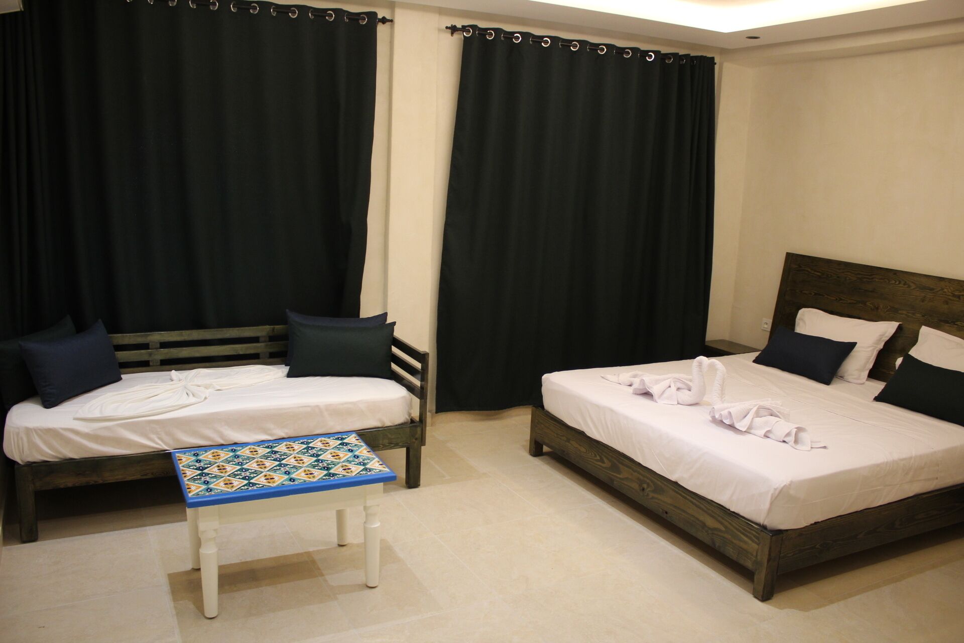 Ein Hotelzimmer mit zwei Betten, einem kleinen Tisch und dunklen Vorhängen.