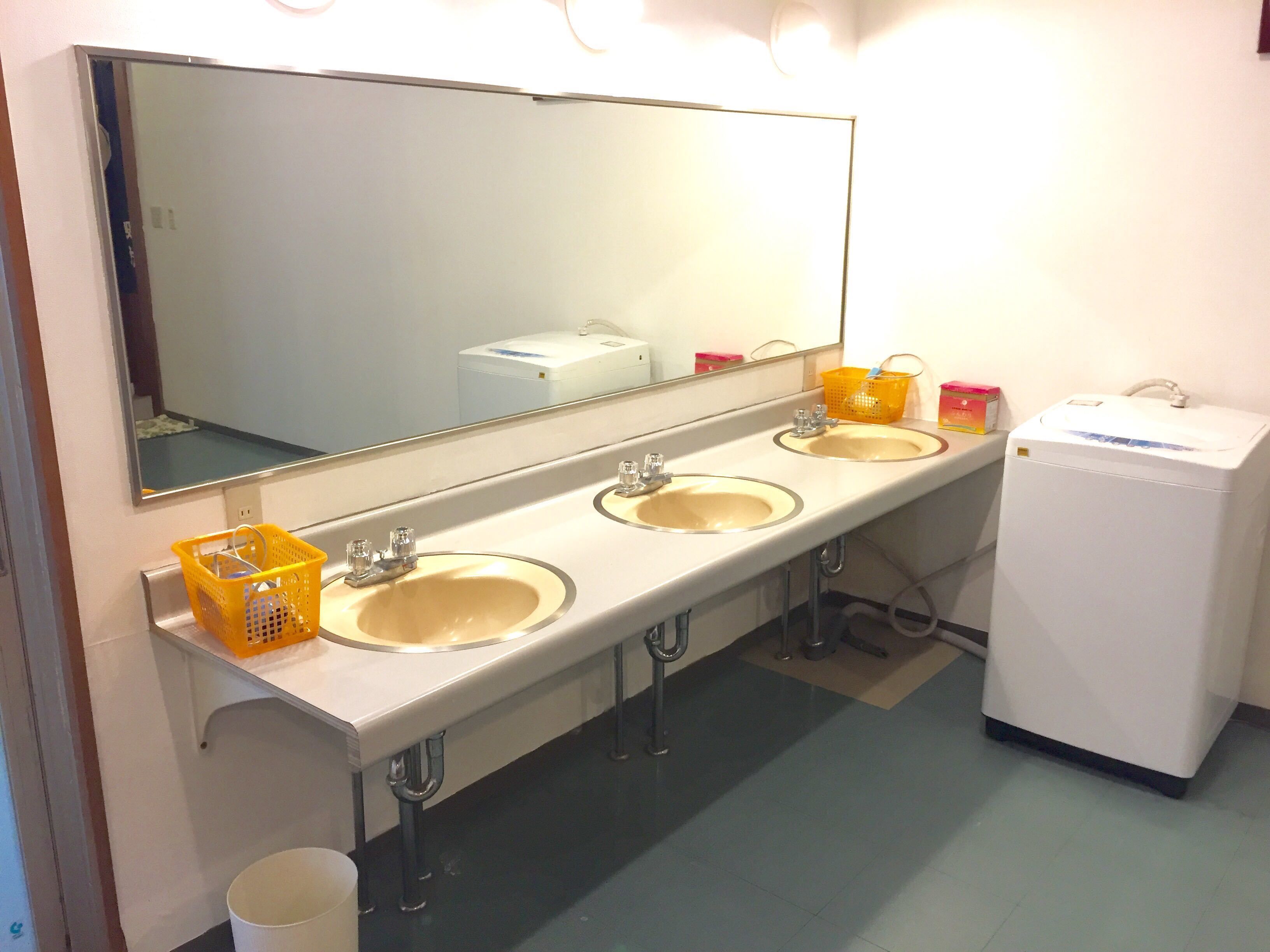 A bathroom with three sinks, a large mirror, and a white refrigerator.