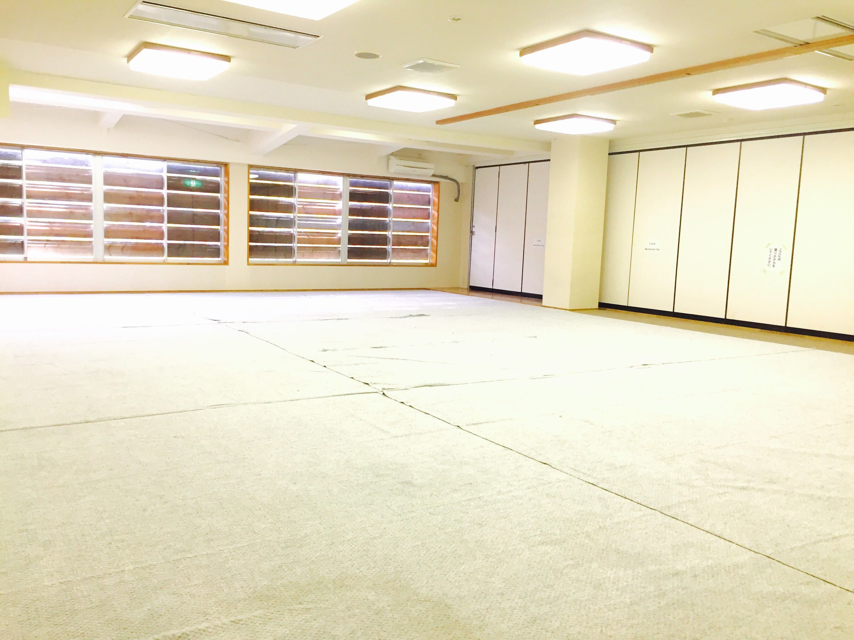 A spacious room with a concrete floor, large windows with blinds, and a wardrobe with multiple doors.