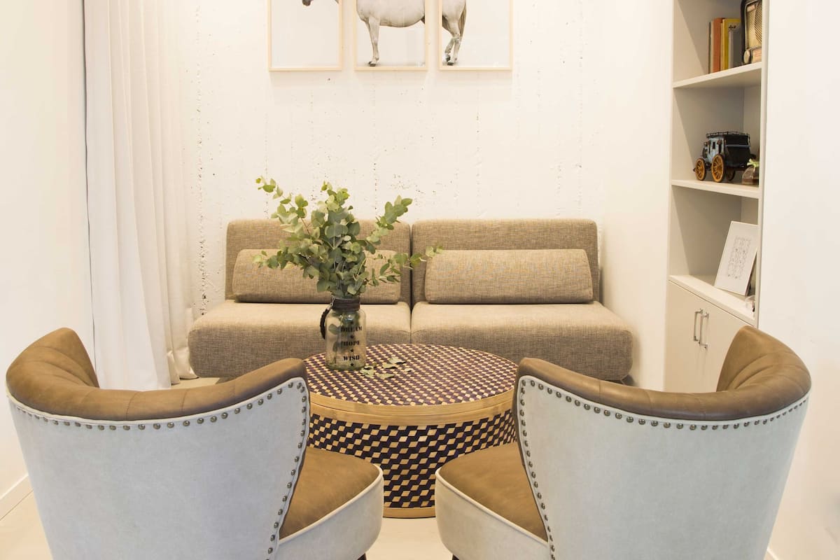 A cozy living room with a sofa, two armchairs, a coffee table, and a bookshelf.