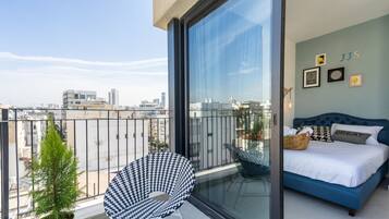 A balcony with a view of the city, a blue bed, and a small potted plant.