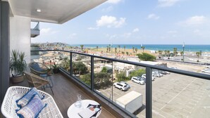 Ein Balkon mit Korbmöbeln, einem Glastisch und Blick auf Strand und Parkplatz.