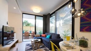 Ein modernes Wohnzimmer mit einer Couch, einem Esstisch, Stühlen, einem Fernseher und einem großen Fenster mit Vorhängen.