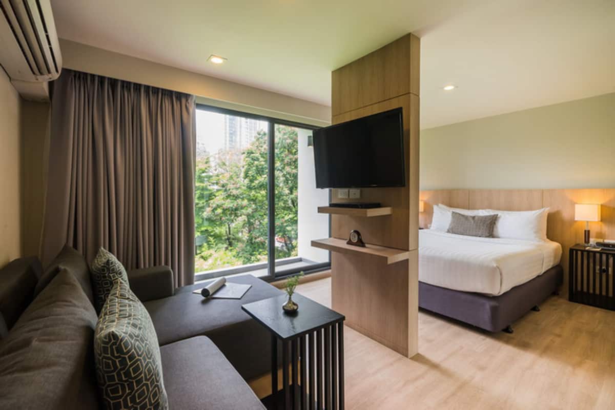 Habitación de hotel moderna con sofá, cama, televisor montado en un panel de madera y vistas a zonas verdes.