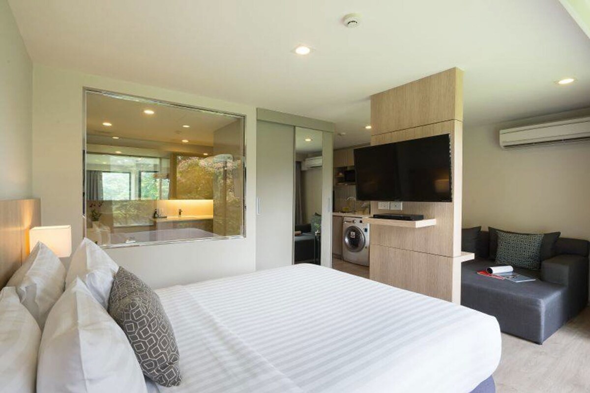 A modern hotel room with a large bed, a TV, a washing machine, and a sofa.