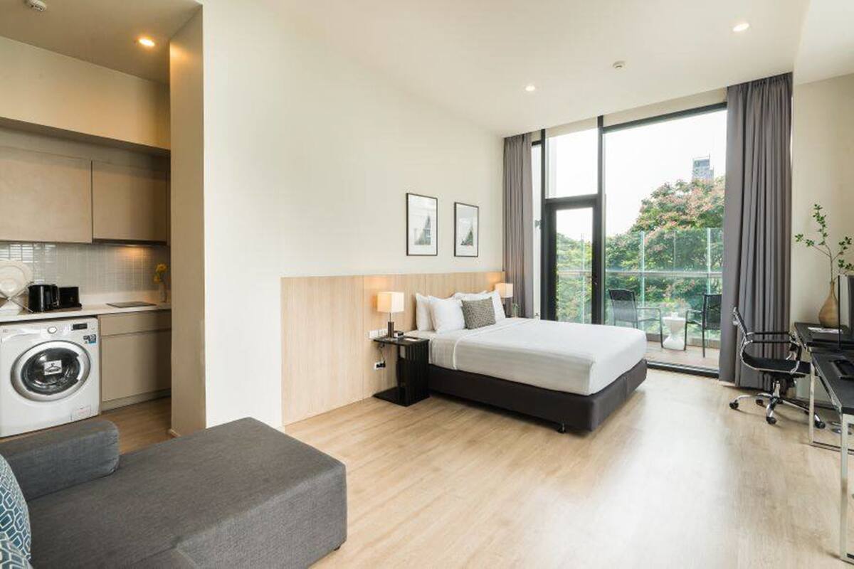 Una habitación de hotel moderna con cama, escritorio, silla, sofá, lavadora y un ventanal con vistas.