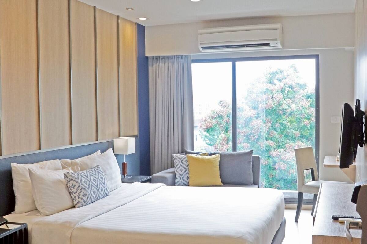 Habitación de hotel moderna con una cama grande, un escritorio y vistas a árboles por la ventana.