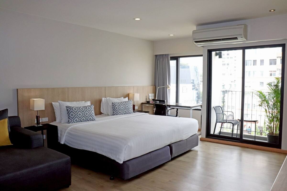 Una habitación de hotel moderna con una cama grande, un escritorio y un balcón con vistas a la ciudad.