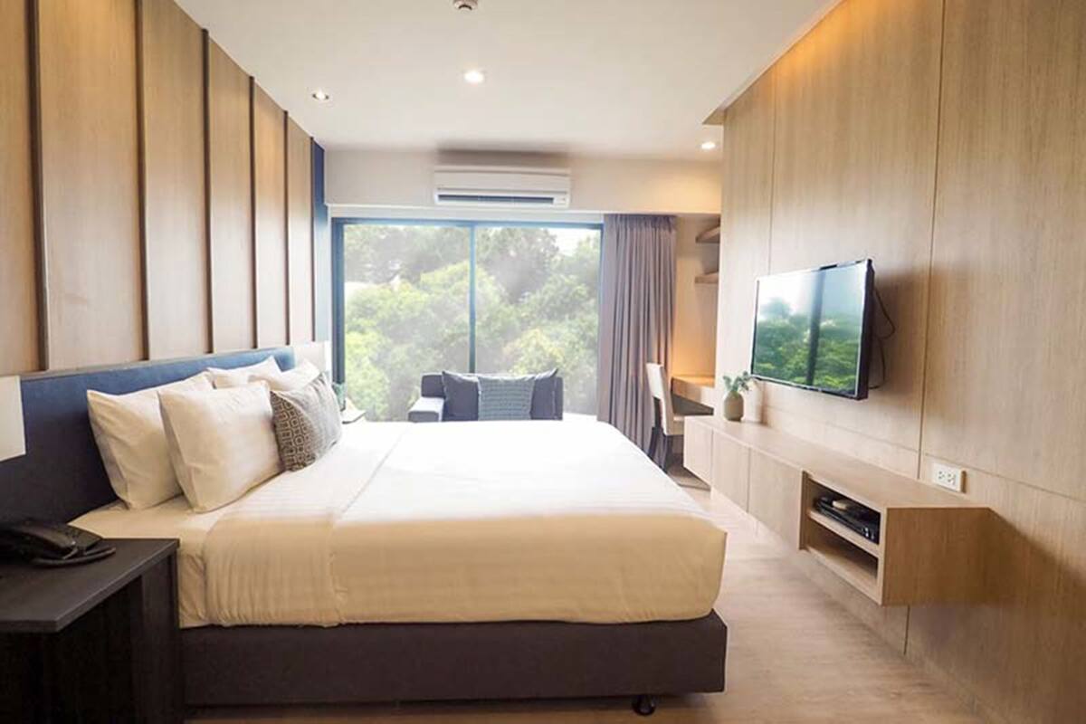 Habitación de hotel moderna con una cama grande, televisión de pantalla plana, escritorio y vistas a zonas verdes por la ventana.
