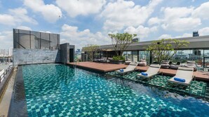 Ein Infinity-Pool auf dem Dach mit Liegestühlen und einem modernen Gebäude im Hintergrund.
